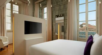 Bright hotel room at Avani Avani Palazzo Moscova Milan Hotel with a white bed, purple pillows, TV panel, large windows, and curtains