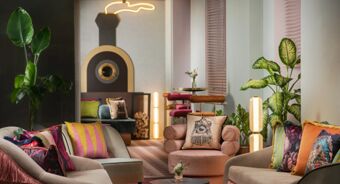 A lounge area with colorful cushions on beige sofas, potted plants, round tables, and a decorative wall piece at Avani Avani Palazzo Moscova Milan Hotel