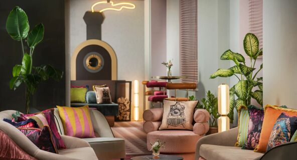 A lounge area with colorful cushions on beige sofas, potted plants, round tables, and a decorative wall piece at Avani Avani Palazzo Moscova Milan Hotel
