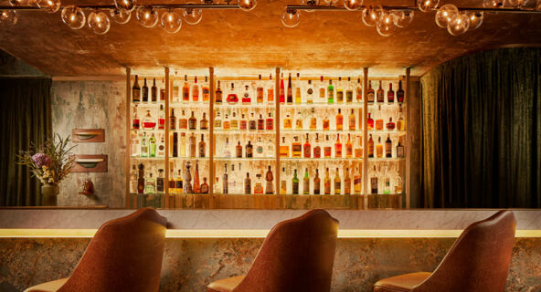 Interior view of a backlit bar displaying various liquor bottles with brown leather chairs in front at Avani Avani Palazzo Moscova Milan Hotel