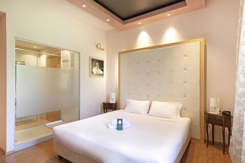 Modern hotel room with white bed, decorative headboard, bedside tables with lamps, and glass enclosed bathroom at B&B Hotel Malpensa Lago Maggiore