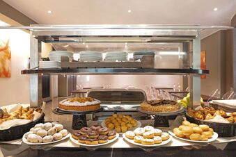 Assorted donuts, muffins, croissants, cakes, and plates displayed on a buffet at B&B Hotel Malpensa Lago Maggiore