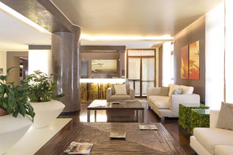 Modern hotel lobby area at B&B Hotel Malpensa Lago Maggiore with white sofas, large plant pots, and wooden coffee tables