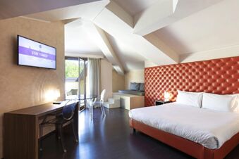 Modern hotel room at B&B Hotel Malpensa Lago Maggiore featuring a double bed with leather headboard and wall-mounted TV