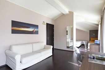 Modern room at B&B Hotel Malpensa Lago Maggiore with white sofa, dark wood flooring, wall mirror, desk, and laptop on table