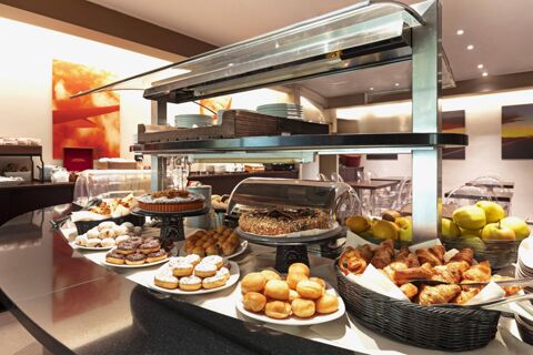 Breakfast buffet display with various pastries, donuts, muffins, fruits, and plates at B&B Hotel Malpensa Lago Maggiore