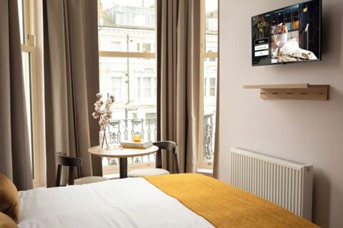 Bright hotel room at Bob W London Holland Park with a bed, yellow throw, small table, two chairs, and wall-mounted TV