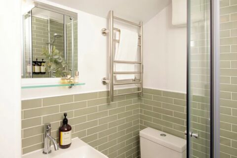 Bathroom in Bob W London Holland Park with light green tiled half walls, a sink, a towel rack, and a glass shower door
