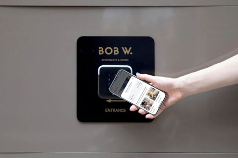 Hand holding a smartphone near a digital lock panel with Bob W London Holland Park logo and entrance text visible
