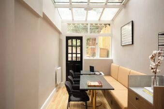 Interior view of a dining area with black chairs, beige bench seating, a chessboard, and a glass ceiling at Bob W London Holland Park