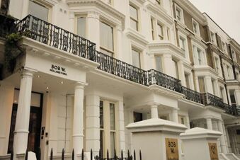 White multi-story building with tall columns and black iron balconies displaying sign Bob W London Holland Park on the facade