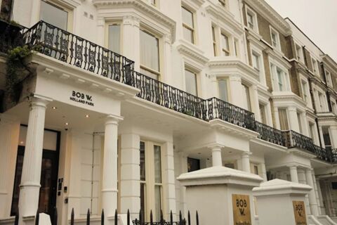White multi-story building with tall columns and black iron balconies displaying sign Bob W London Holland Park on the facade
