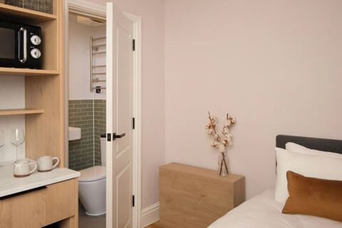 Small hotel room at Bob W London Holland Park featuring a partially open bathroom door, wooden shelves, bed, and decorative vase