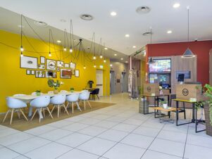 Reception area and seating with white chairs, tables, hanging lights, yellow wall decor, and B&B Hotel Milano-Monza desks
