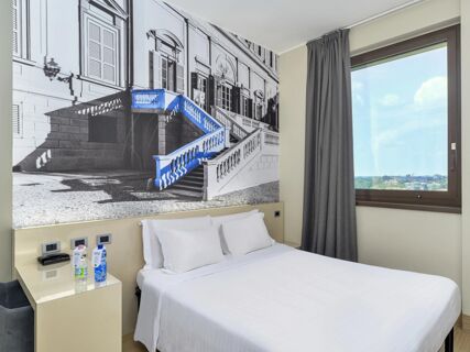 Bed with white linens and two pillows below a large black and white wall photo with a blue staircase at B&B Hotel Milano-Monza