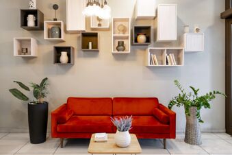 Red velvet sofa with cylindrical armrests below wooden decorative shelves with vases and books in B&B Hotel Milano-Monza