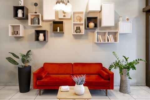 Red velvet sofa with cylindrical armrests below wooden decorative shelves with vases and books in B&B Hotel Milano-Monza