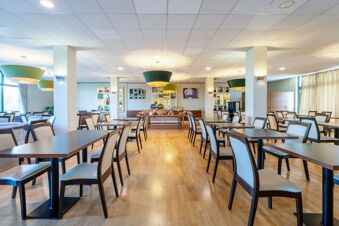 Dining area with wooden tables and chairs, green pendant lights, and buffet setup at B&B Hotel Expo Verona Villafranca