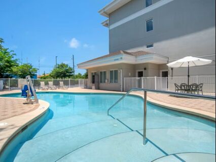 Outdoor swimming pool with metal handrails, lounge chairs, tables with umbrellas, and a multi-story building at Garner Hotel Panama City Beach Northeast