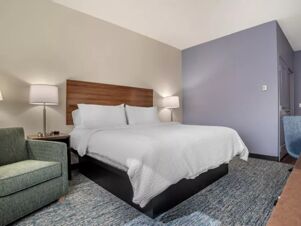 A clean hotel room at Garner Hotel Panama City Beach Northeast featuring a king-size bed, green armchair, and two lamps on nightstands