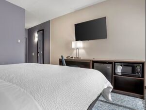 Hotel room at Garner Hotel Panama City Beach Northeast featuring a white bed, wall-mounted TV, desk, chair, lamp, mini fridge, and microwave