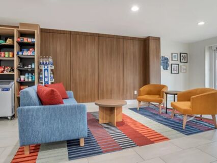 A seating area at Garner Hotel Panama City Beach Northeast with a light blue sofa, two orange chairs, a round wooden table, and a colorful striped rug