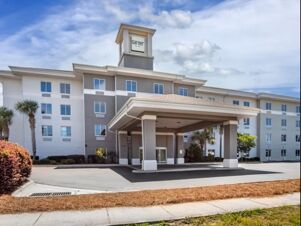 Modern four-story Garner Hotel Panama City Beach Northeast building with covered entrance, palm trees, and clear sky above