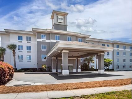 Modern four-story Garner Hotel Panama City Beach Northeast building with covered entrance, palm trees, and clear sky above
