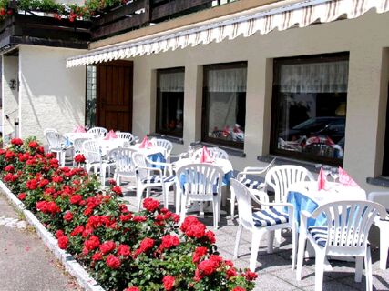 White plastic chairs and tables set with blue and white linens on the Gasthof Kranz patio next to red flowers