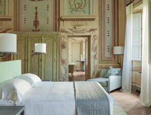 Bedroom interior with a white bed, green armchair, floor lamps, and frescoed walls at COMO Castello Del Nero Hotel & Spa