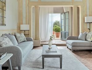 Living area with gray sofas, a wooden coffee table, a white vase, and an open door to a terrace at COMO Castello Del Nero Hotel & Spa