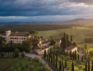 COMO Castello Del Nero Hotel & Spa surrounded by cypress trees and rolling green hills under a cloudy sky
