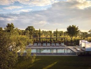 Outdoor swimming pool with sun loungers and pergola surrounded by trees and greenery at COMO Castello Del Nero Hotel & Spa
