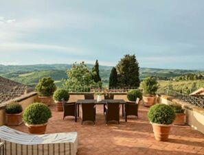 Terrasse mit Esstisch und Sitzpl&auml;tzen, umgeben von Topfpflanzen und Blick auf die h&uuml;gelige Landschaft beim COMO Castello Del Nero Hotel & Spa.