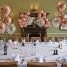 A table set for a celebration with wine bottles, glasses, lit lamps, and rose gold balloons reading 50 and 40 at Hotel du Vin Cheltenham