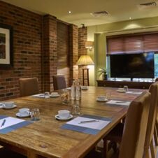 A conference room with a wooden table, chairs, notepads, cups, a TV, and lamps at Hotel du Vin Cheltenham