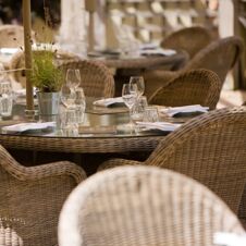 Outdoor dining table with glass top set with glassware, napkins, and menus surrounded by wicker chairs at Hotel du Vin Cheltenham