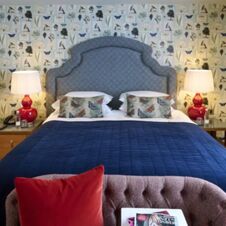 A bedroom in Hotel du Vin Cheltenham featuring a blue quilted bedspread, patterned pillows, butterfly wallpaper, and bedside lamps