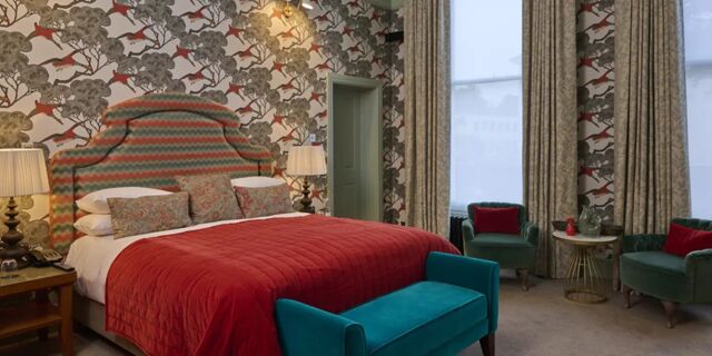 Hotel du Vin Cheltenham bedroom with patterned headboard, red quilted bedspread, green chairs, and large windows with curtains