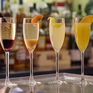 Four cocktail glasses with assorted fruit garnishes lined up on a tray at Hotel du Vin Cheltenham bar with bottles in background