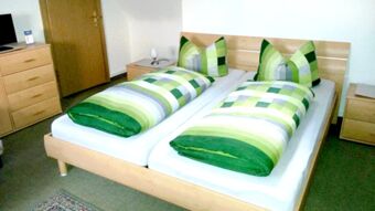 Helles und schlicht eingerichtetes Schlafzimmer mit Doppelbett und gr&uuml;n karierten Bettdecken in der Pension Arnold.
