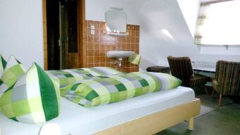 Gem&uuml;tliches Zimmer mit gr&uuml;n karierten Bettdecken, Waschbecken mit braunen Fliesen und Sitzbereich bei Pension Arnold.