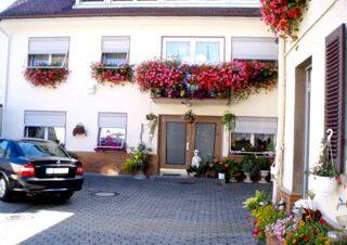 Hof mit Eingang und blumengeschm&uuml;ckten Fenstern der Pension Arnold, einladend und gepflegt mit geparktem Auto und Pflanzen.
