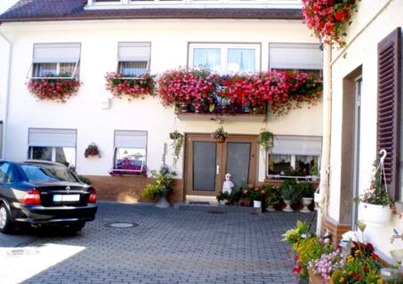 Hof mit Eingang und blumengeschm&uuml;ckten Fenstern der Pension Arnold, einladend und gepflegt mit geparktem Auto und Pflanzen.