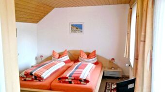 Gem&uuml;tliches Schlafzimmer mit gepolsterten Betten und orangen Bettw&auml;sche in der Pension Arnold, hell und einladend gestaltet.
