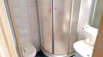 Kleines Badezimmer mit Duschkabine, Toilette und Waschbecken in der Pension Arnold, hell und funktional eingerichtet.