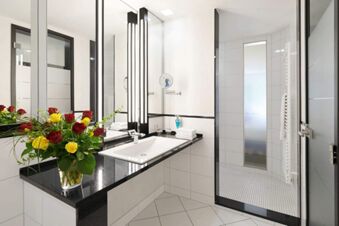 Bathroom sink area at Landhotel Krone with black countertop, red and yellow roses in a glass vase, and a walk-in shower