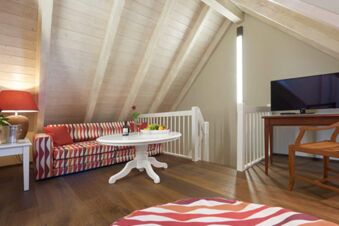 A living room at Landhotel Krone with patterned sofa, white round table, wooden chair, TV on wooden desk, and slanted wood ceiling beams