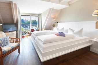 Bright hotel room at Landhotel Krone with double bed, wooden floor, armchairs, TV, and balcony with outdoor seating