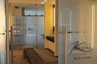 Glass doors with frosted panels and the Landhotel Krone wellness logo lead to a spa area with wooden benches and stone floors